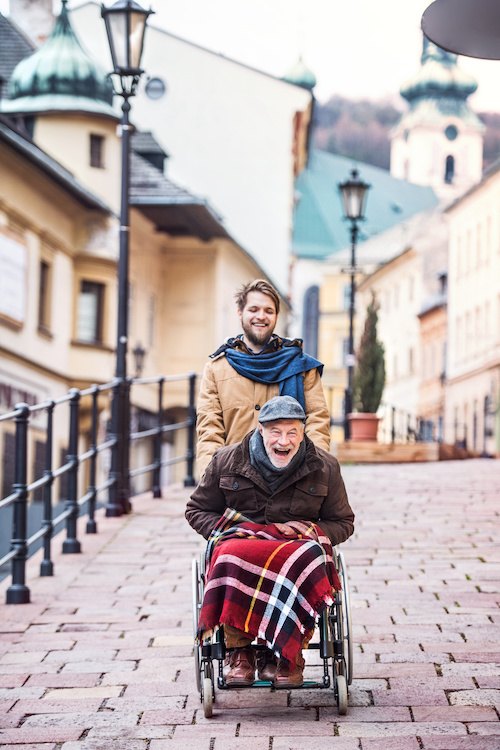 Senior father in wheelchair and young son on a walk.